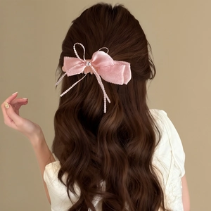 Détail d'une pince à cheveux avec nœud en dentelle rose sur longs cheveux ondulés
