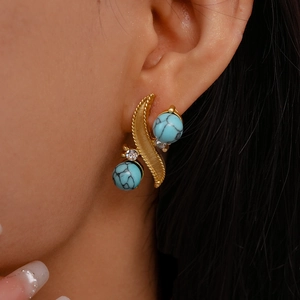 Detailed close-up of golden vintage-style earrings with turquoise stones and rhinestones