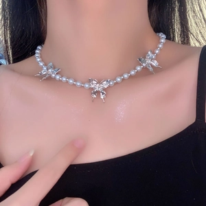 Detailed view of pearl necklace featuring three silver butterfly pendants on a model