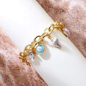 Detail of gold ocean charm bracelet with starfish, seashell, and pearl on textured sand
