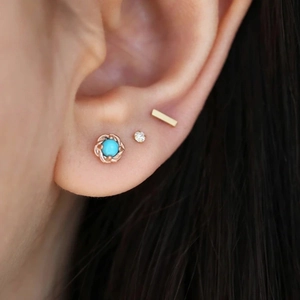 Detailed view of turquoise flower stud with gold bar and diamond piercing set on ear