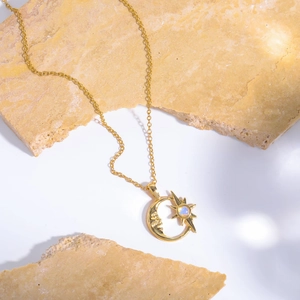 Detailaufnahme des Goldanhängers mit Sonne, Mond und Opal auf Travertin-Fliesen