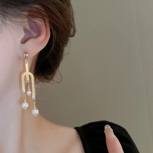 Close-up of unique gold fork-shaped earrings with pearls worn on ear for elegant style