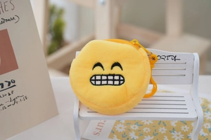Detail of yellow plush coin purse with embroidered smiling emoji and yellow plastic hook