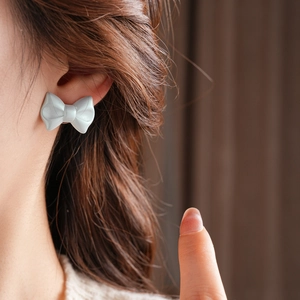 Close-up of light blue acrylic bow stud earrings with a matte finish on a model
