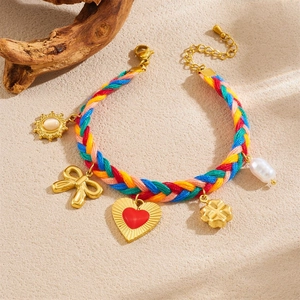 Rainbow braided rope bracelet with gold heart and sun pendants on a sandy background