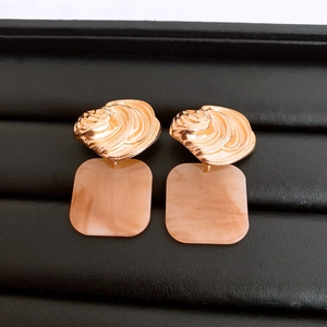 Macro shot of French luxury square gold earrings with nude resin charms on black display