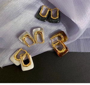 Detail of U-shaped gold earrings with black, amber, and white resin rectangle drops