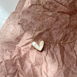 Minimalistische Goldkette mit Perlmutt-Herzanhänger auf braunem Papierhintergrund