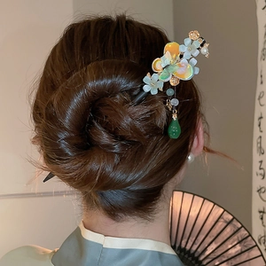 Close-up of floral hair pin with blue beads, pearls, and a green tassel in a hairstyle