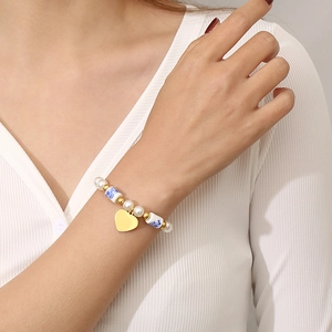 Bracelet en perles avec motifs floraux bleus et pendentif coeur porté au poignet