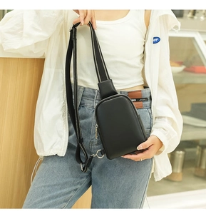 Detail of minimalist black leather chest bag featuring silver zipper and white stitched strap