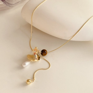 Detail of tiger eye stone pendant and white pearl on a delicate gold layered necklace chain