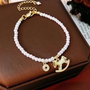 Dettaglio ravvicinato del bracciale di perle con ciondoli a forma di pony e moneta