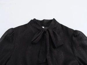 Détail du décolleté d'une robe en mousseline noire avec nœud élégant et tissu texturé