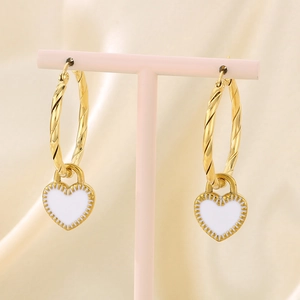 Close-up of golden twisted hoop earrings with white enamel heart pendants on a display stand