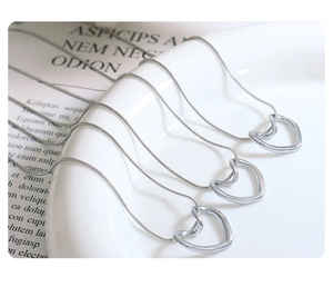 Three silver heart pendant necklaces on snake chains displayed on a ceramic tray