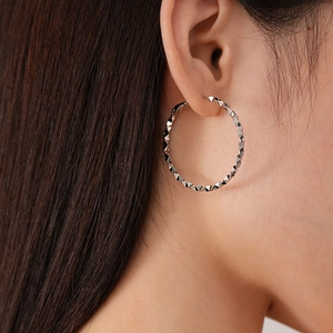 Macro shot of silver geometric faceted hoop earring showing prismatic light reflection