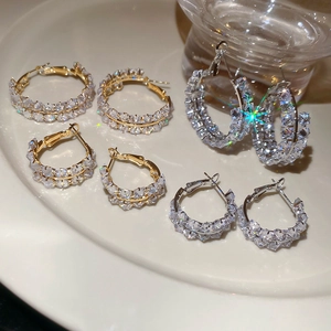 Détail de boucles d'oreilles créoles dorées et argentées serties de zircons cubiques