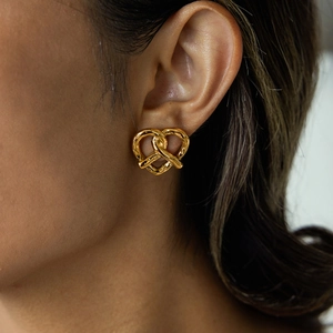 Close-up of golden bow-shaped stud earrings worn by a model in soft lighting
