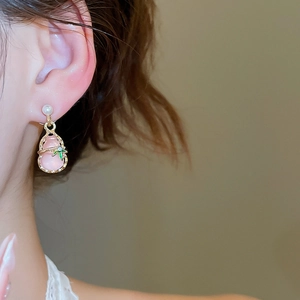 Close-up of pink gourd drop earring with pearl stud on model in natural lighting