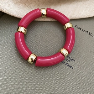 Detail of magenta acrylic tube beads and gold spherical metal spacers on a geometric bracelet