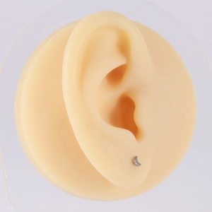 Macro shot of silver crescent moon stud earring worn on a silicone ear model