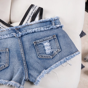 Dettaglio degli shorts di jeans blu con frange e spalline in nastro intrecciato