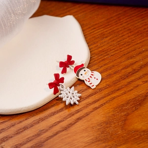 Christmas asymmetric snowman and red bow earrings on wooden texture background
