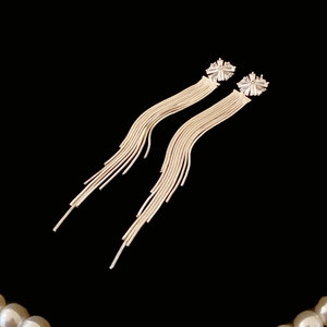 Macro shot of gold tassel earrings with zircon flower studs against black background