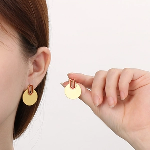 Elegant gold-tone circular stud earrings with red enamel accent worn by model