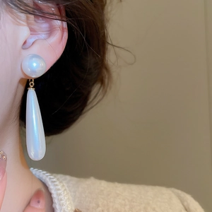 Close-up of elegant long teardrop pearl earrings worn by model with gold link detail