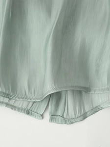 Close-up of light green silk-like fabric showing neat stitching and soft褶wrinkles