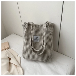 Detail view of beige corduroy tote bag with 'You need this one' label on a cozy bed