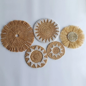 Detail of five bohemian hand-woven straw wall decors with white cotton embroidery and tassels