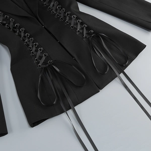 Detail of waist cross-tie design with metal eyelets and satin ribbons on a black blazer dress