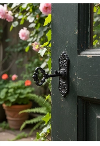 Détail d'une poignée clé rétro en fonte noire installée sur une porte de jardin en bois vert