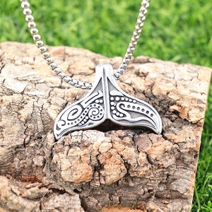 Polished silver Viking whale tail pendant necklace with swirl patterns on natural bark