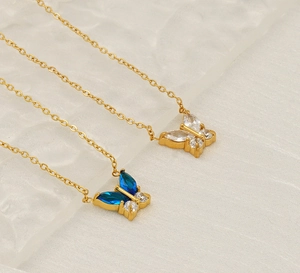 Close-up of golden butterfly pendants with blue and white zircon on glass surface