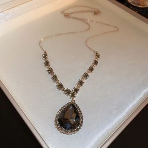 Gros plan d'un collier long en V or rose avec une pierre grise taillée en poire dans un écrin