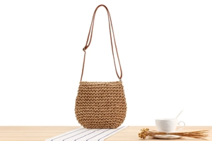 Close-up of woven straw shoulder bag with natural texture and brown strap on wooden table