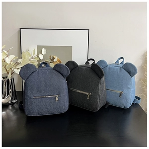 Three colors of denim mini backpacks with bear ears on a desk in a cozy indoor setting