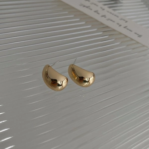 Macro detail of golden teardrop bean earrings with glossy metallic finish and C-shape design