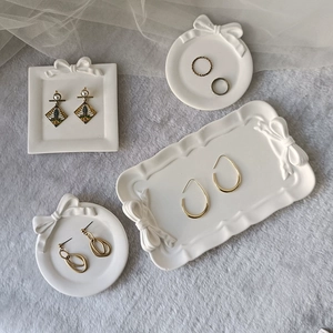 Bow-knot resin tray mold displaying various gold pearl earrings and rings on mesh fabric