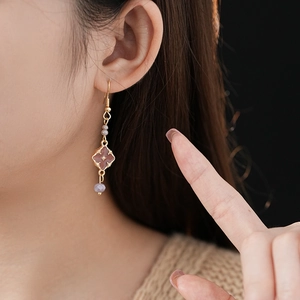 Detail of vintage gold drop earrings with pink diamond charms and grey beads on model
