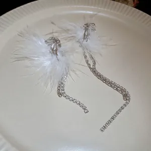 Silver fringe earrings with white feathers and sparkling rhinestones on ceramic dish