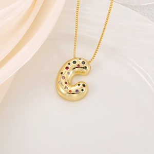Macro detail of gold letter C pendant necklace with colorful cubic zirconia on silk