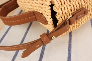 Detail of woven straw texture with brown leather strap and metal buckle on crossbody bag