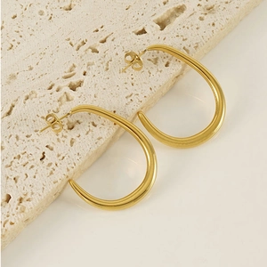 Detail of 18K gold-plated U-shaped stainless steel earrings on a beige stone surface