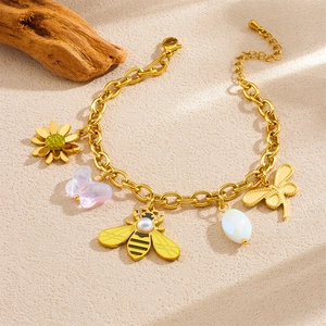 Gold stainless steel bracelet with colorful butterfly, bee and flower charms on sand surface